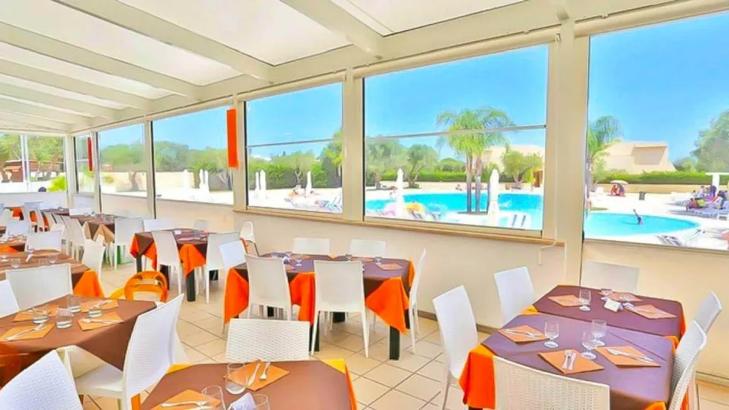 Sala ristorante interna con tavoli apparecchiati e ampie vetrate affacciate sulla piscina