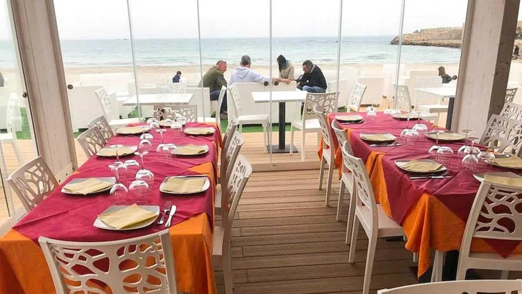 Sala ristorante con vista mare, tavoli apparecchiati con tovaglie rosse e arancioni