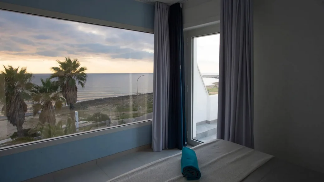 Camera con ampia vetrata panoramica sul mare e palme al tramonto
