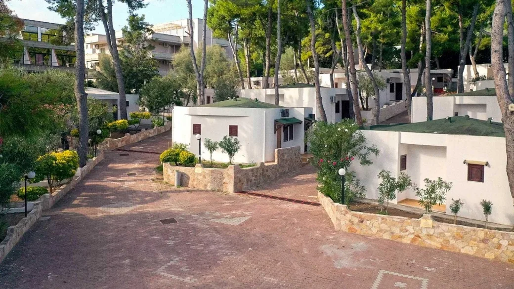 Vialetto pavimentato tra bungalow bianchi con tetto verde immersi nel verde