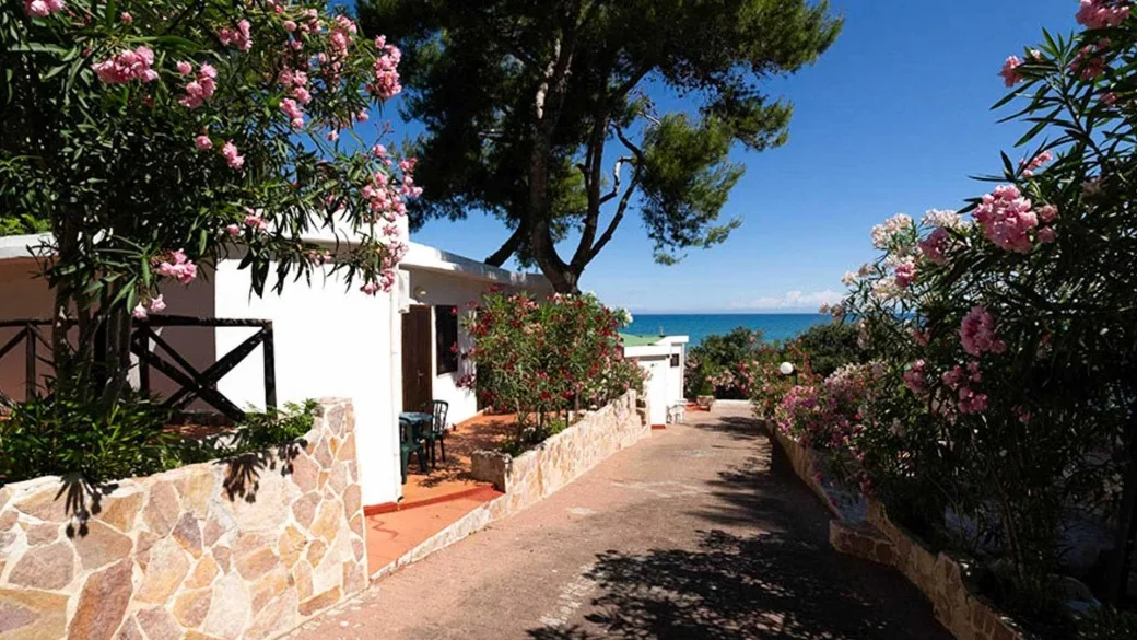 Vialetto tra bungalow bianchi con oleandri fioriti e vista mare