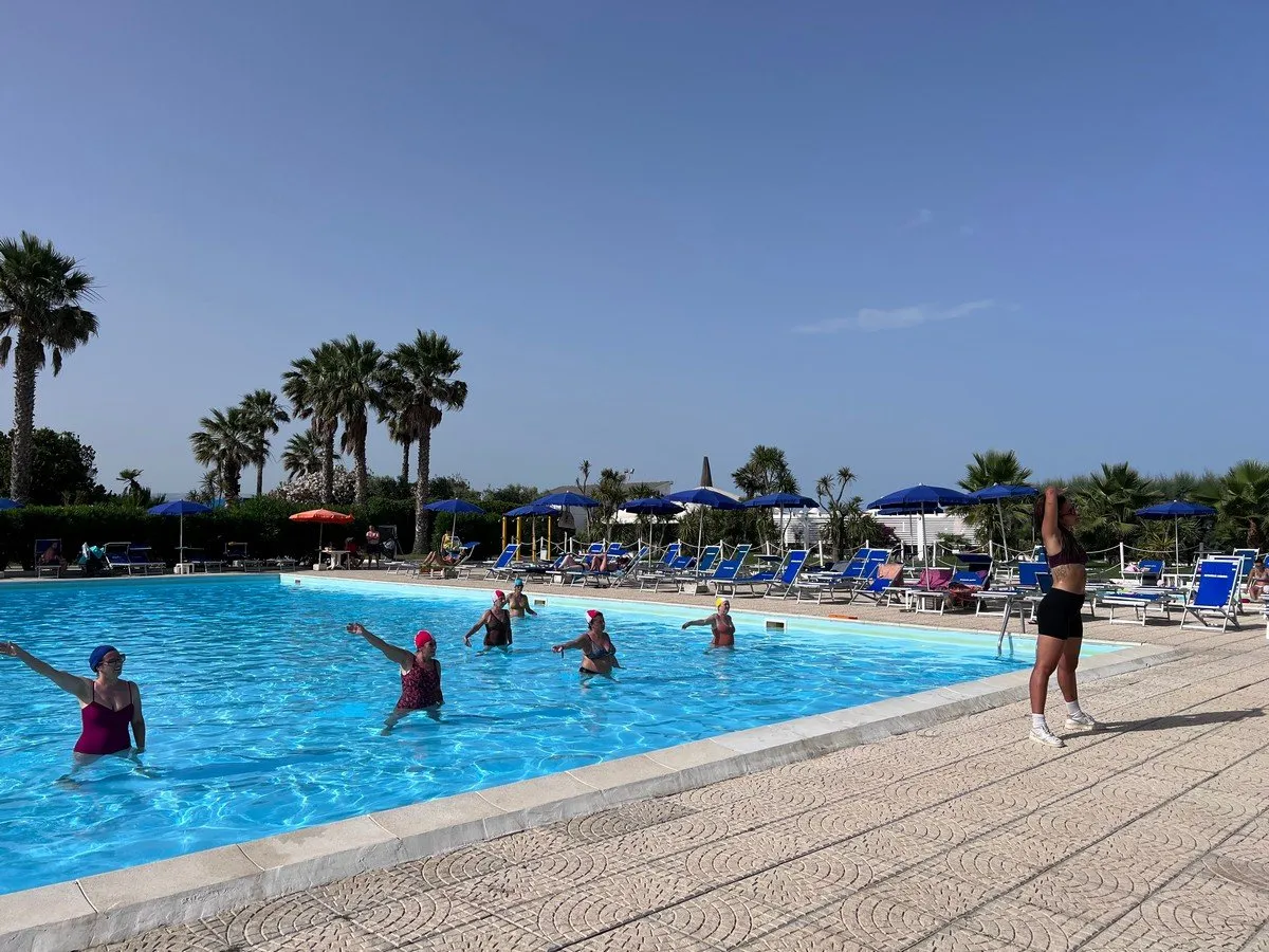 Lezione di acquagym in piscina con partecipanti e istruttrice a bordo vasca