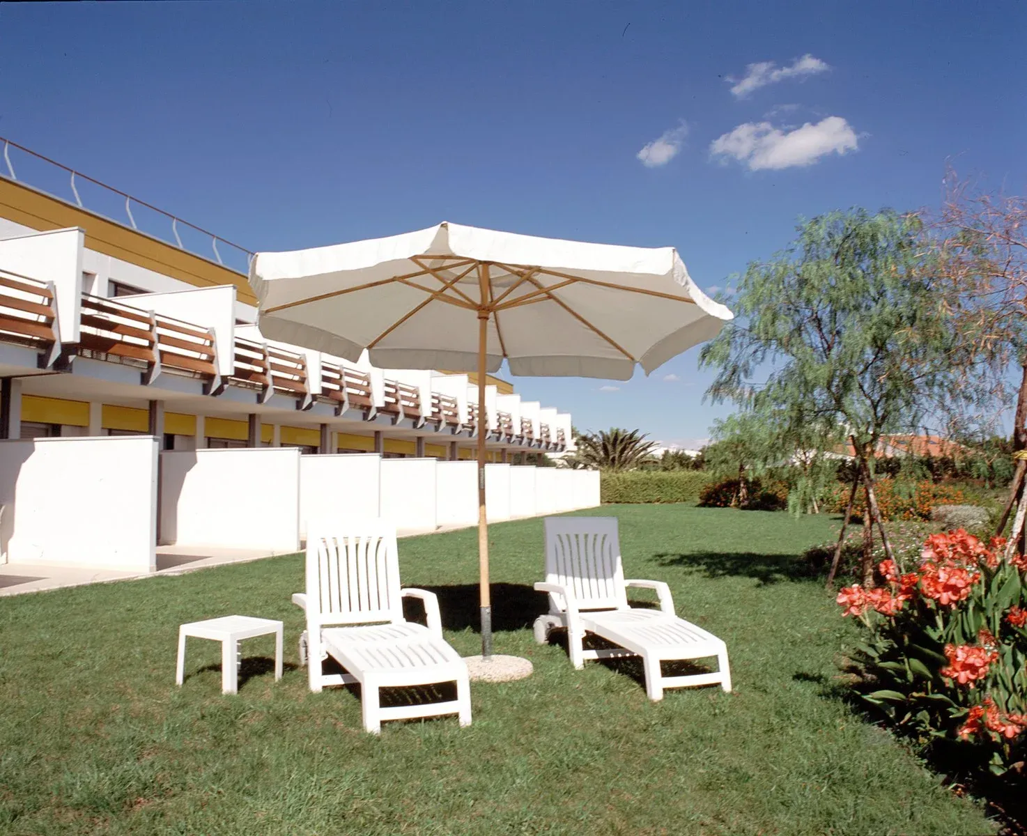 Giardino con lettini bianchi, ombrellone e terrazze delle camere