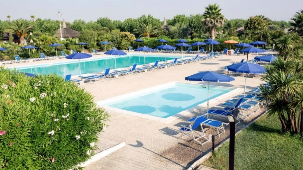 Veduta dall'alto di due piscine con lettini e ombrelloni blu tra il verde