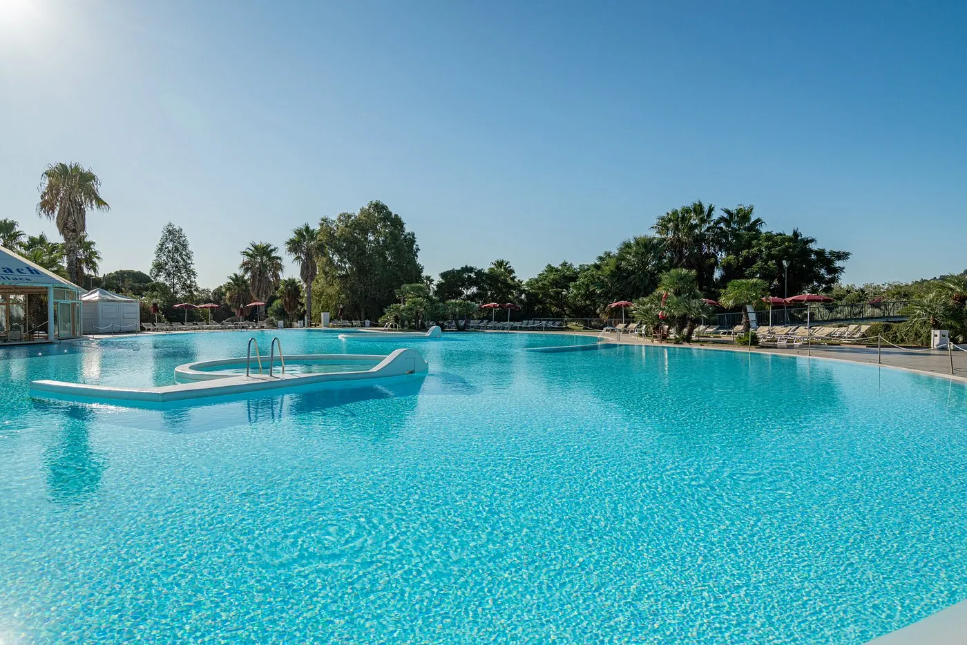 Ampia piscina azzurra del resort circondata da palme e lettini