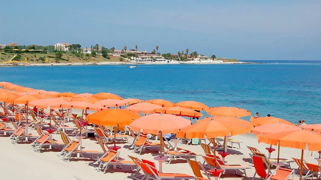 Spiaggia di sabbia con ombrelloni arancioni e mare azzurro