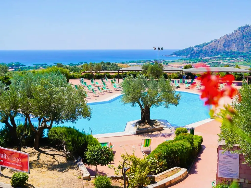 Piscina del resort con lettini, ulivi e vista panoramica sul mare