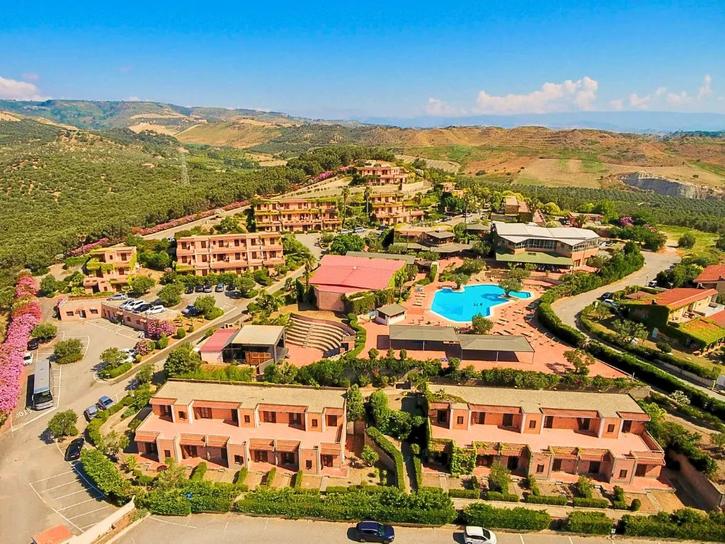 Veduta aerea del resort con edifici, piscina e colline verdi sullo sfondo