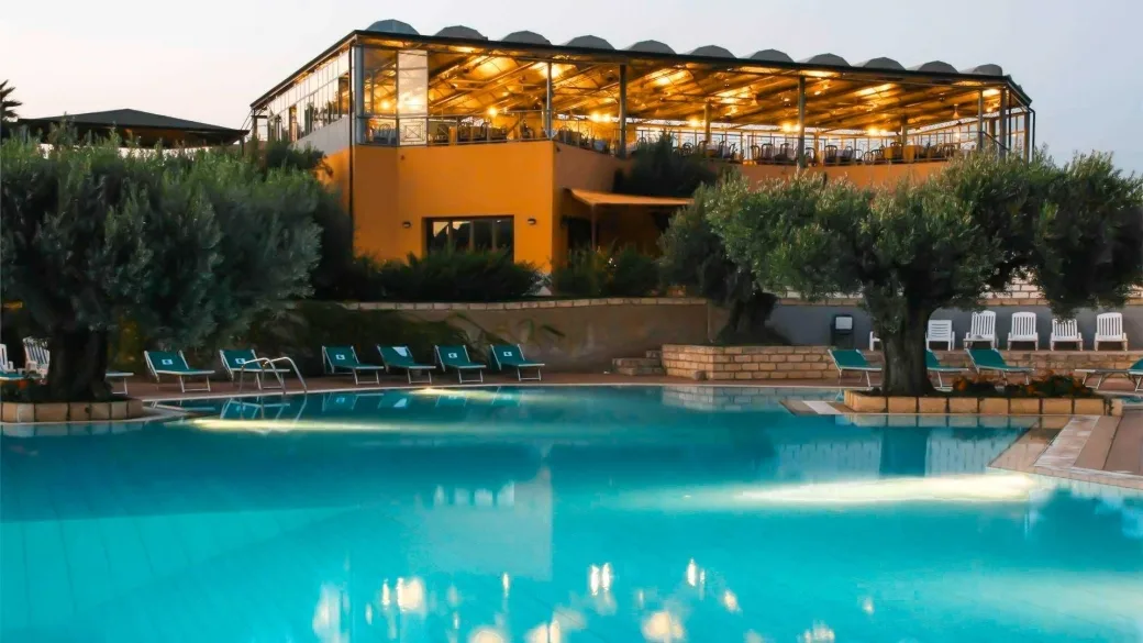 Piscina illuminata al tramonto con ristorante panoramico e ulivi