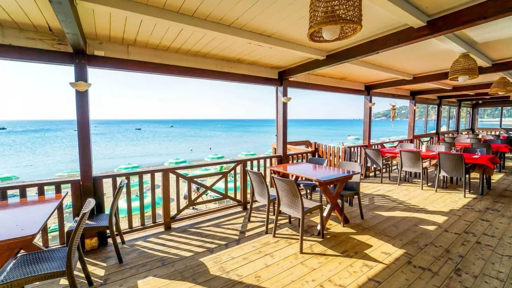 Terrazza ristorante in legno con vista mare e tavoli apparecchiati