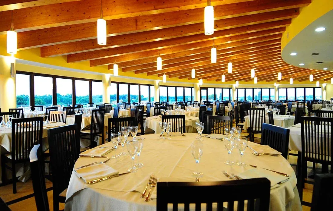 Sala ristorante luminosa con tavoli rotondi apparecchiati e grandi finestre