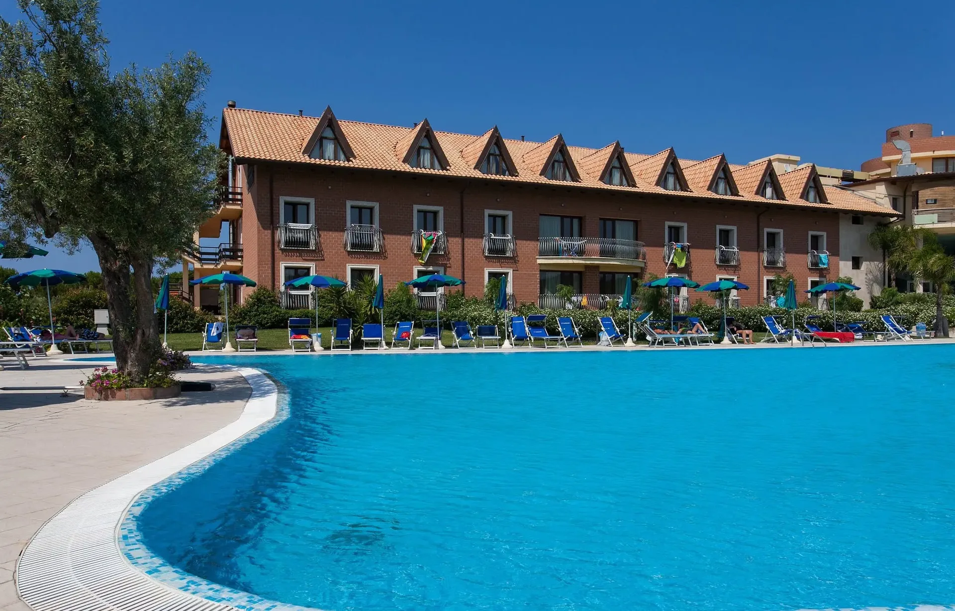 Edificio del resort in mattoni con piscina azzurra e lettini in primo piano
