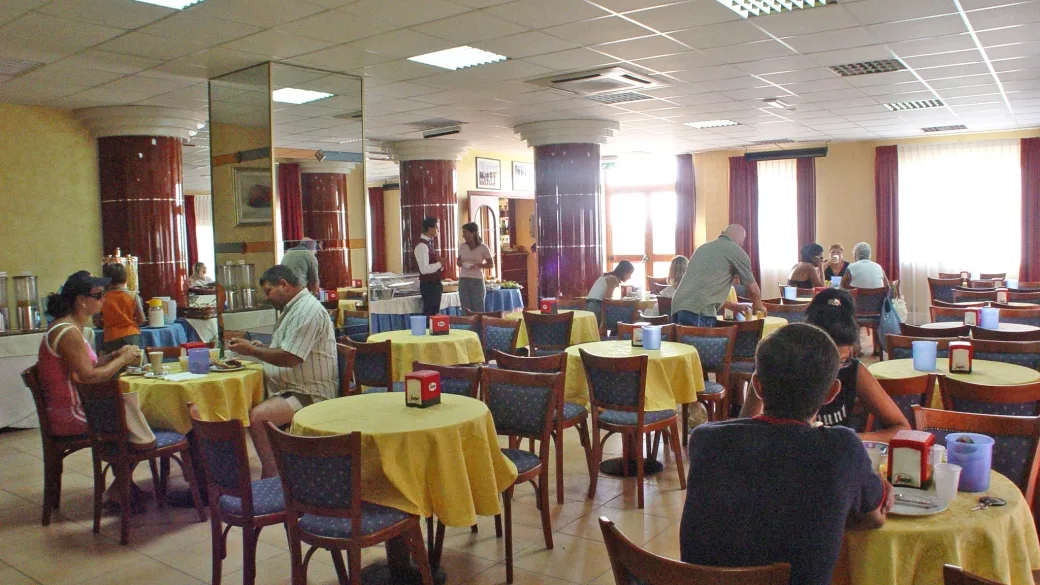 Sala ristorante dell'hotel con tavoli rotondi gialli, sedie e ospiti durante il pasto