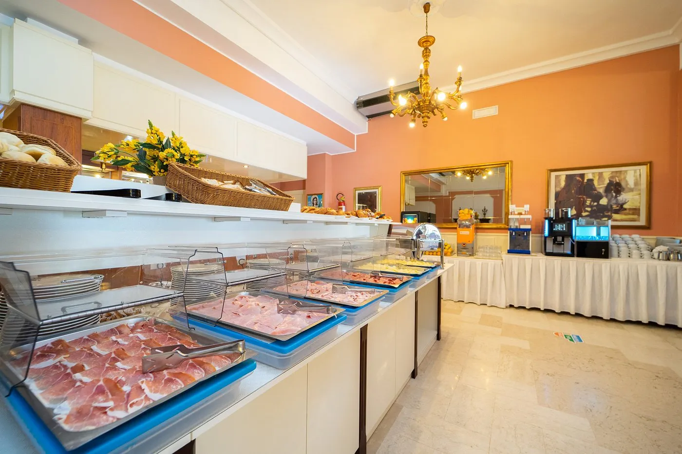 Buffet con salumi, spremuta d'arancia e cornetti in sala colazione