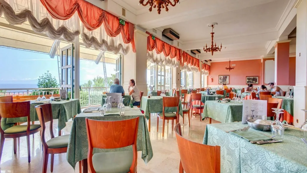 Sala ristorante con tavoli apparecchiati e vista sul mare