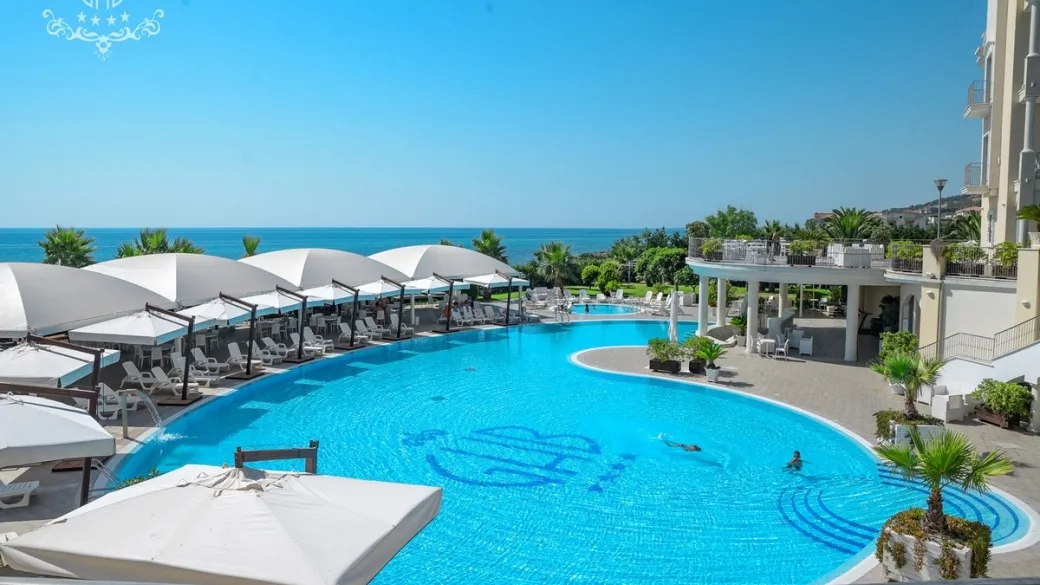 Grande piscina del resort con gazebo bianchi e vista sul mare