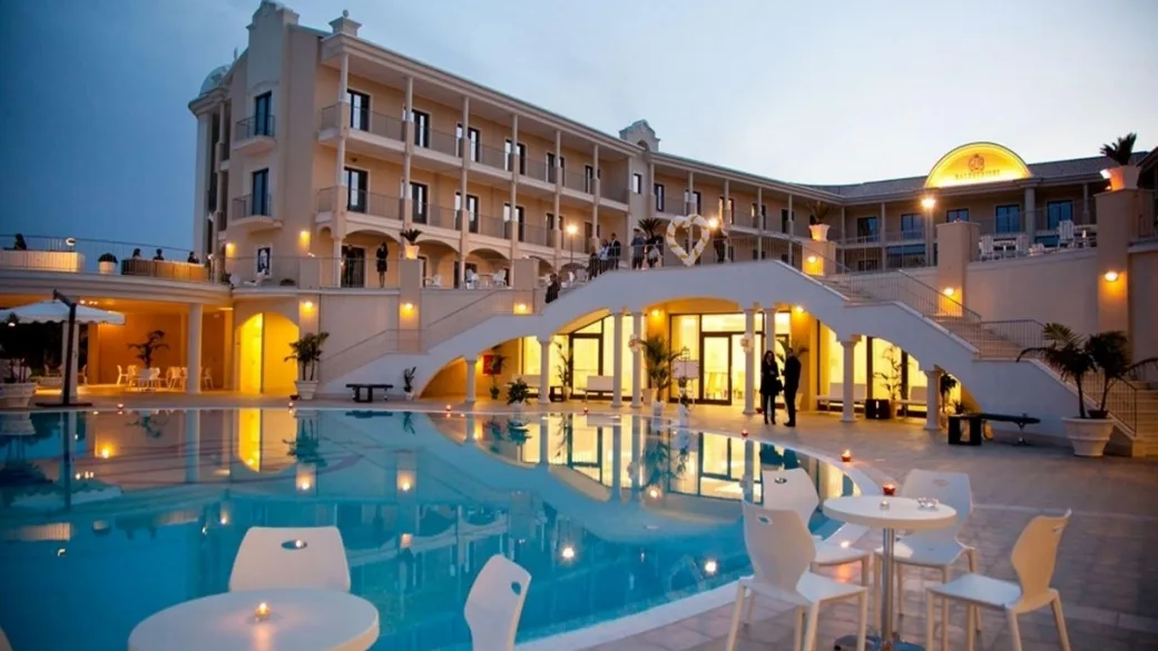 Facciata dell'hotel al crepuscolo con piscina illuminata e scalinata