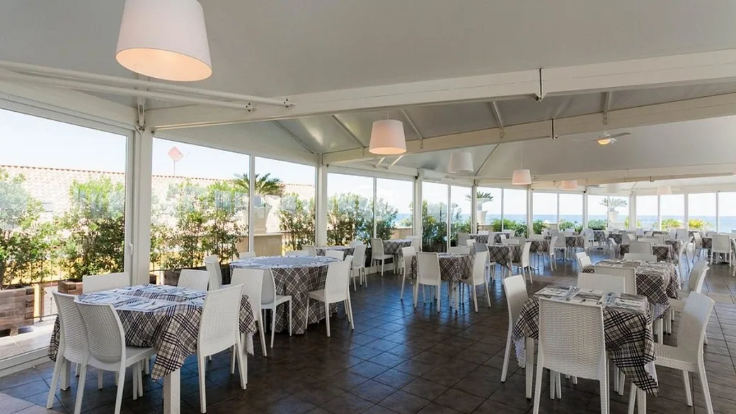 Sala ristorante luminosa con grandi vetrate e tavoli apparecchiati vista mare