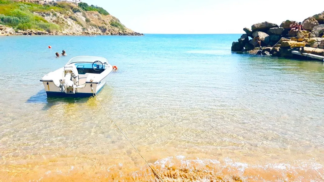 Piccola baia con barca ormeggiata e acqua cristallina tra le rocce