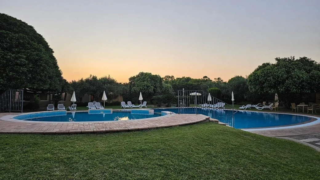 Piscina al tramonto con lettini, ombrelloni e prato verde