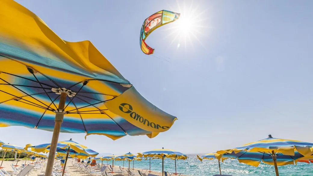 Ombrelloni gialli in spiaggia con kite in volo e sole splendente