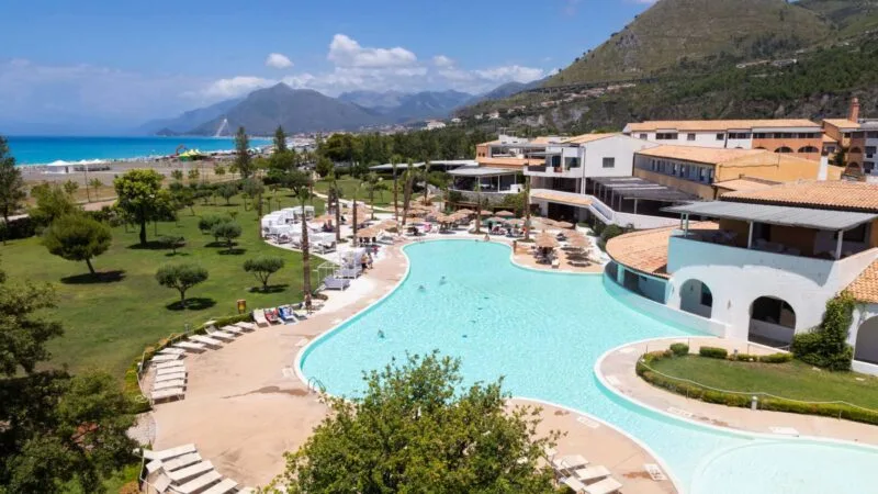 Piscina all'aperto con ombrelloni e lettini, vicino al mare e alle montagne.