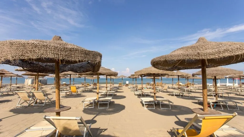 Spiaggia con ombrelloni di paglia e sdraio, vista mare e cielo sereno.