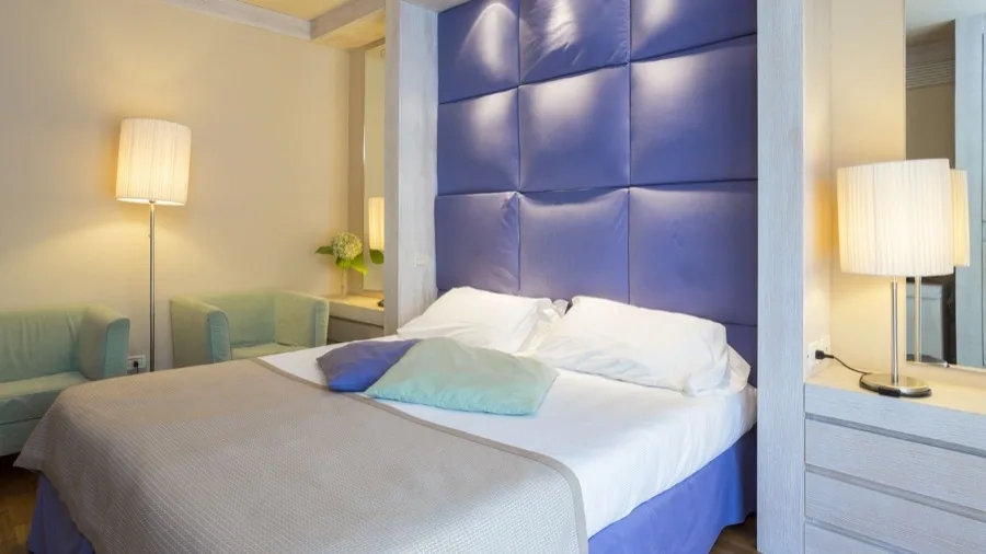 Camera da letto con letto matrimoniale, testiera imbottita blu, due poltrone verdi, due lampade da tavolo e comodini.