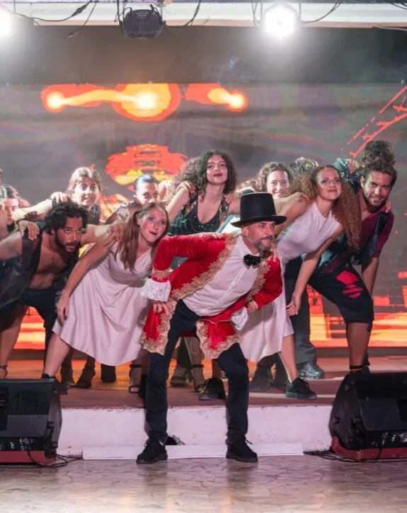 Attori in scena con costumi colorati durante una performance teatrale vivace e coreografata.