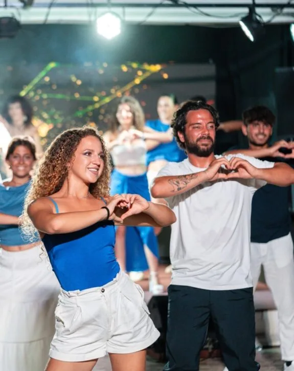 Gruppo di giovani che ballano e formano cuori con le mani durante una performance sul palco.