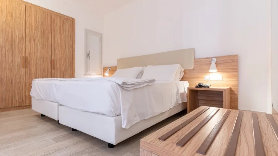Camera da letto moderna con letto matrimoniale bianco, comodini e armadio in legno chiaro, illuminazione calda.