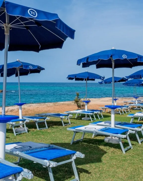 Lettini blu e ombrelloni sulla spiaggia, con vista sul mare turchese sotto un cielo sereno.