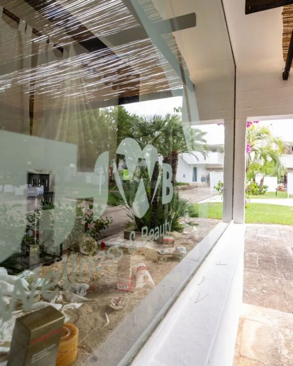 Vetrina di un centro benessere con il logo "Wellness & Beauty" e decorazioni sabbiose, vista da un'angolazione esterna.
