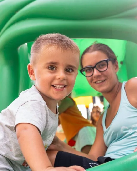 Bambino sorridente e ragazza con occhiali in un parco giochi gonfiabile verde.
