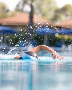 Nuotatore con cuffia bianca e nera che nuota a stile libero in piscina con schizzi d'acqua visibili.