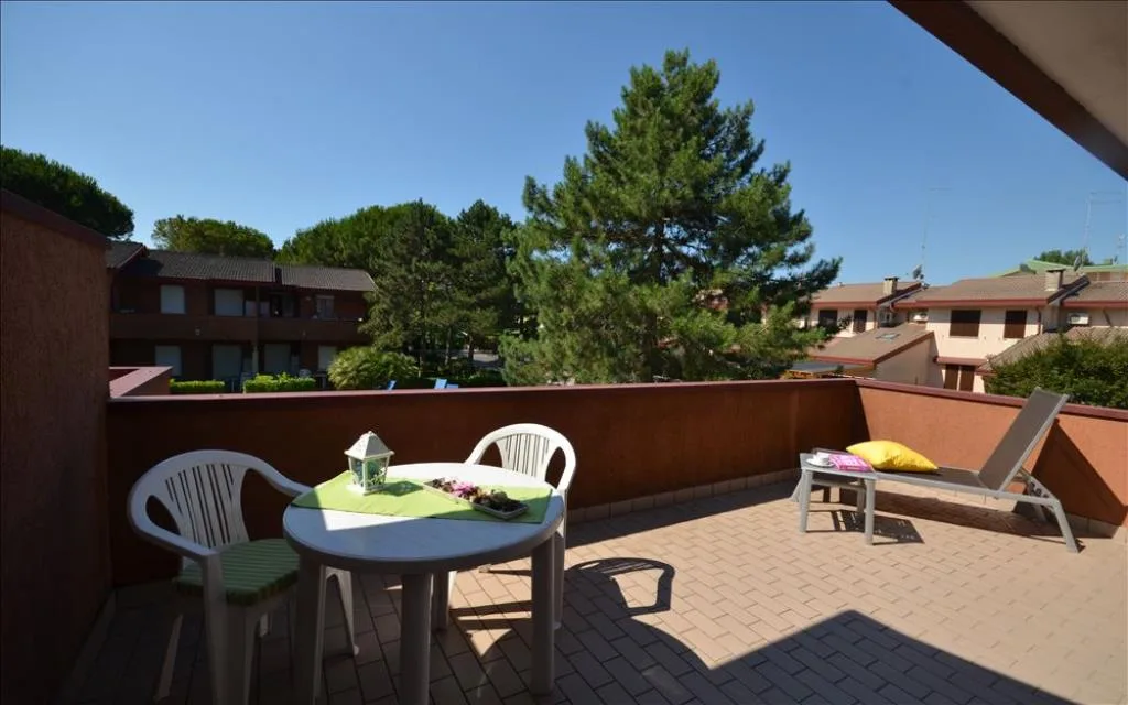 Terrazza con tavolo, sedie e lettino affacciata sul verde del residence