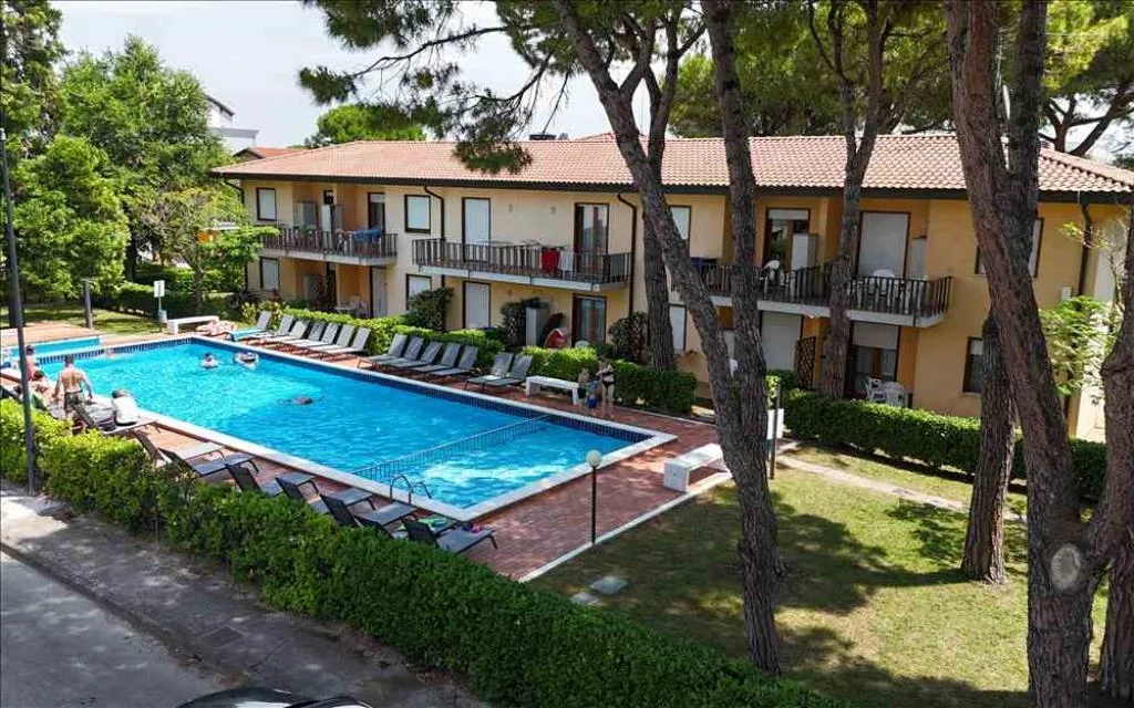 Piscina con lettini e residence giallo circondato da alberi