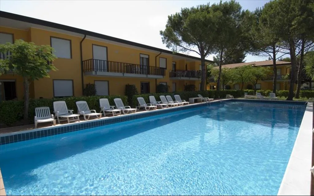 Piscina con lettini bianchi allineati lungo il residence giallo