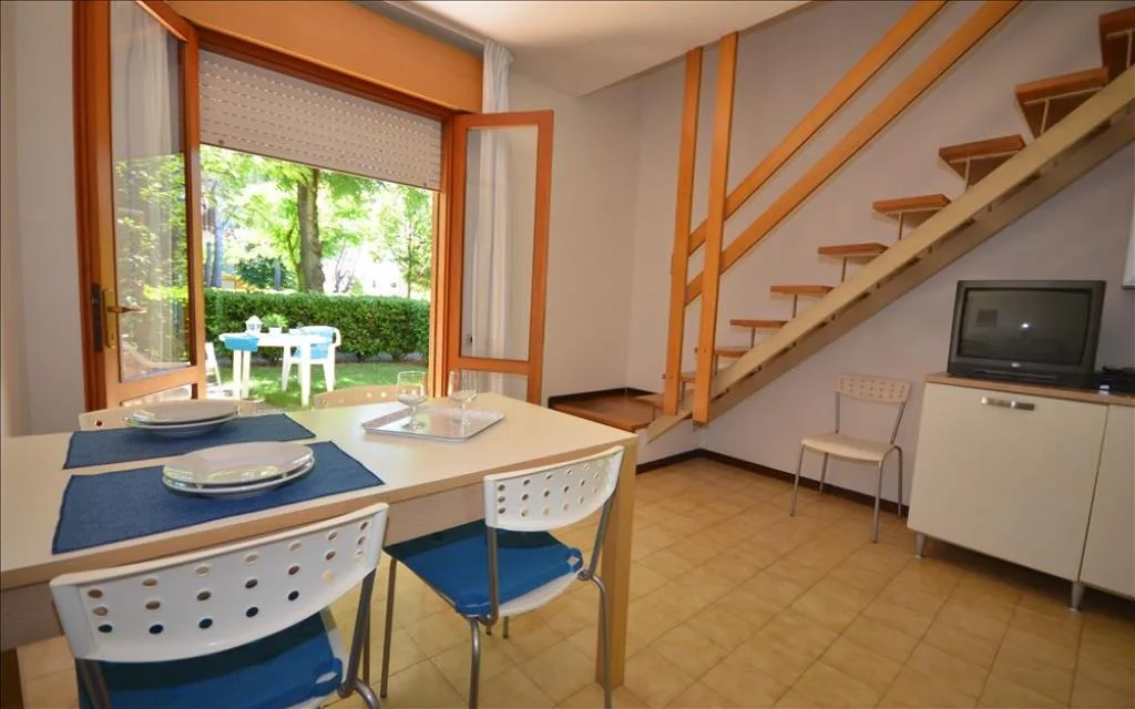 Zona pranzo con tavolo, scala interna in legno e affaccio sul giardino