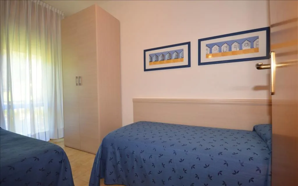 Camera con due letti singoli blu, armadio e finestra luminosa