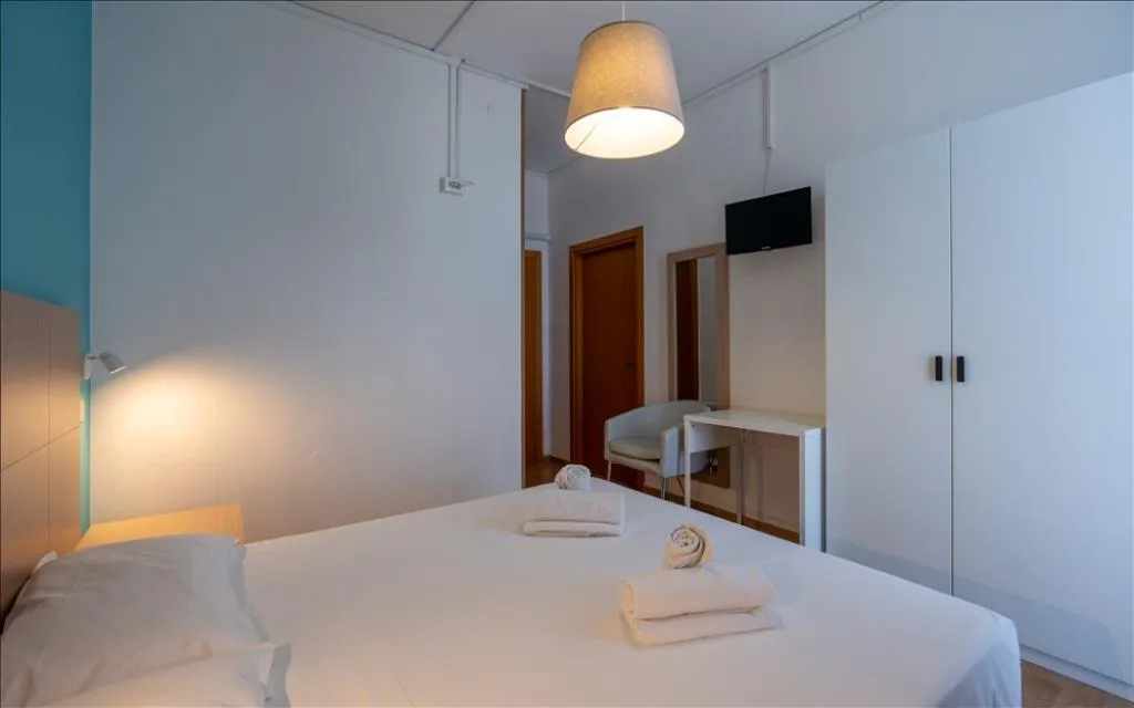 Camera luminosa con letto matrimoniale, scrivania, armadio bianco e TV