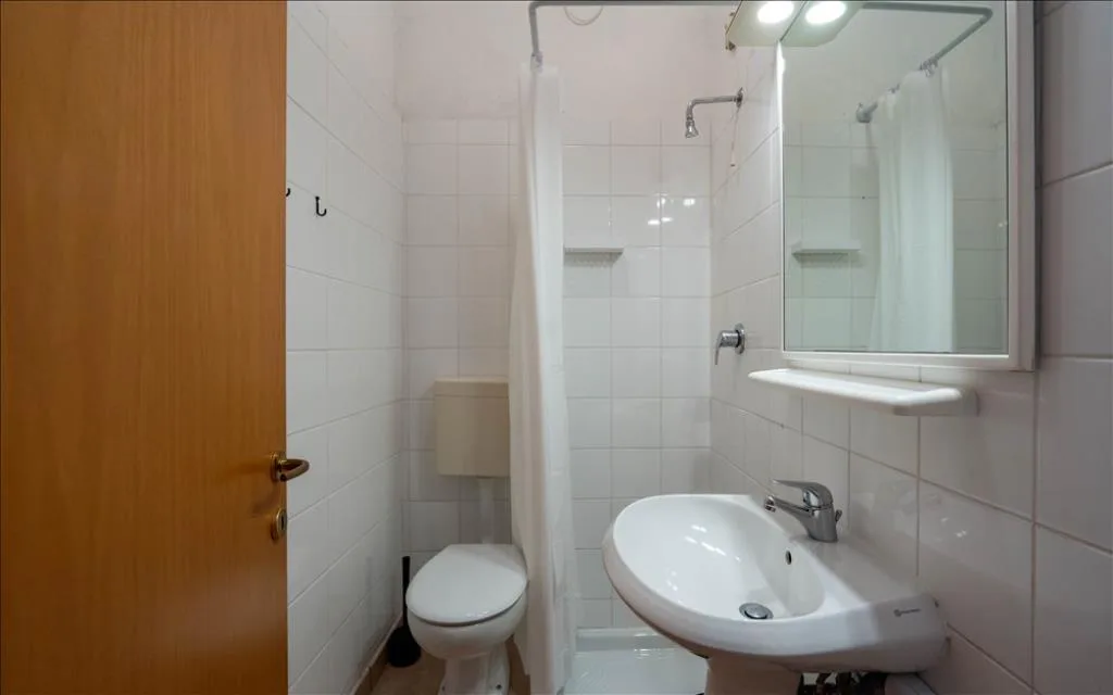 Bagno con lavabo, WC e doccia con tenda, pareti in piastrelle bianche