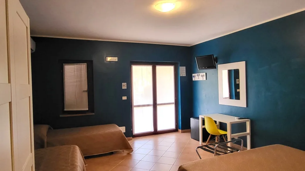 Camera moderna con pareti blu, letti singoli, scrivania e porta finestra