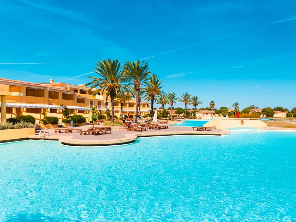 Grande piscina turchese con palme e edificio giallo del resort sotto un cielo azzurro
