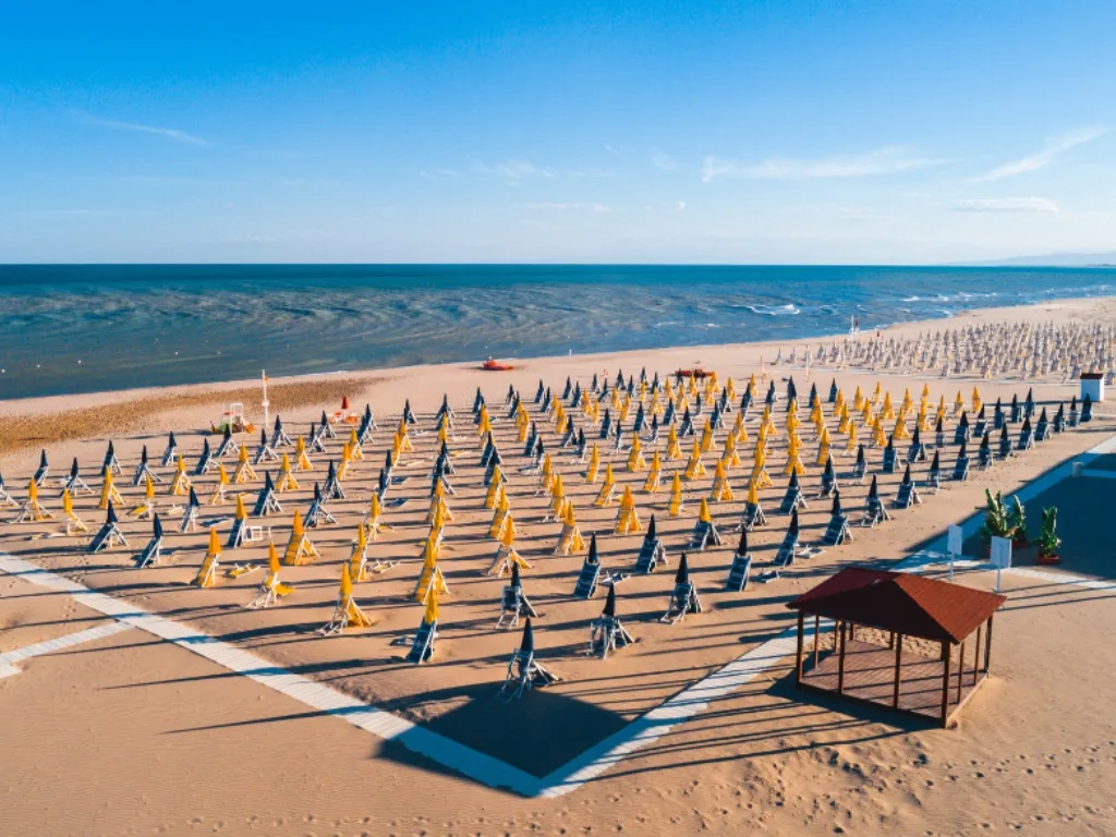Spiaggia di sabbia con file di ombrelloni gialli e lettini affacciata sul mare