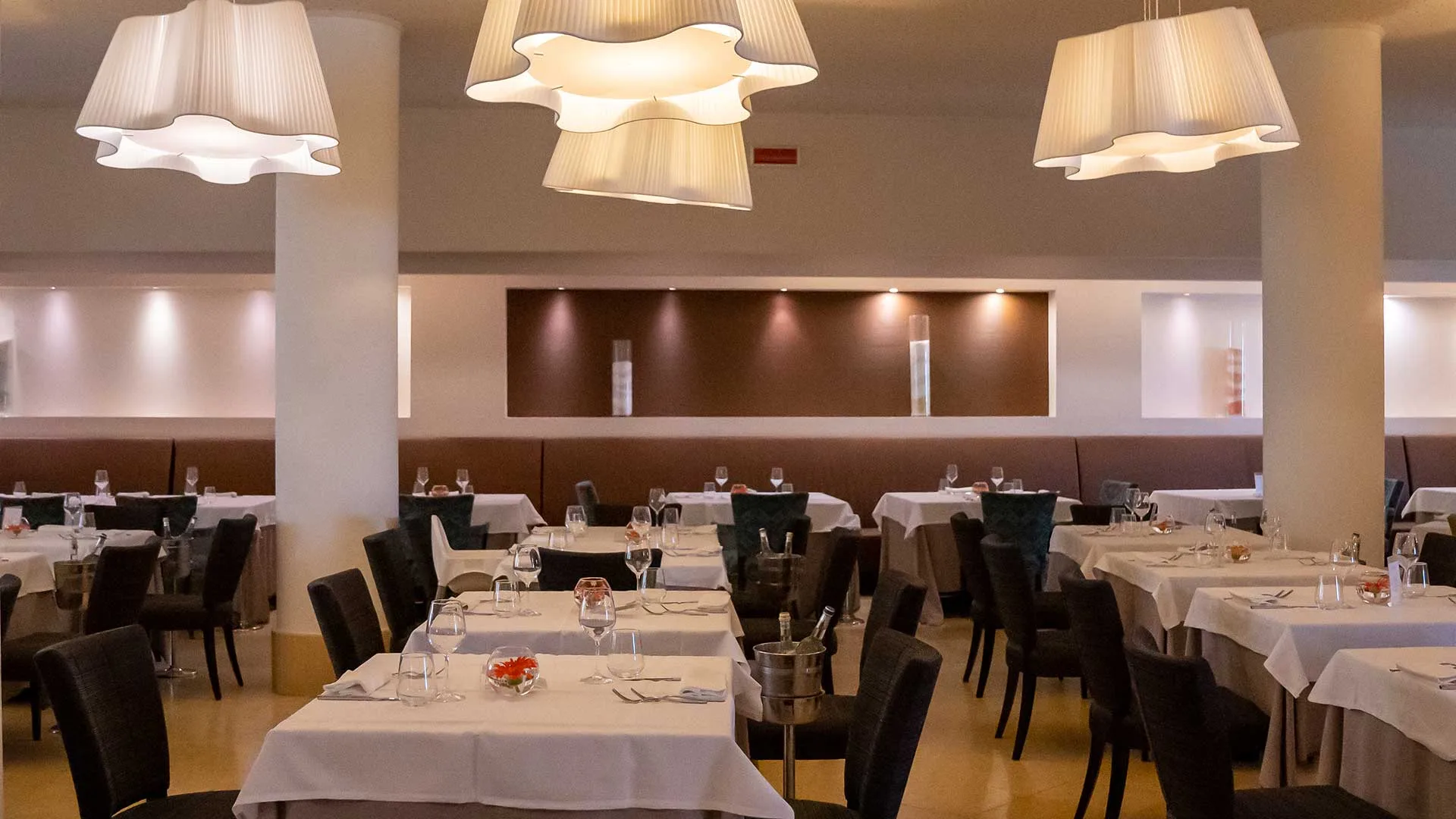 Sala ristorante interna con tavoli apparecchiati, lampadari bianchi e illuminazione soffusa