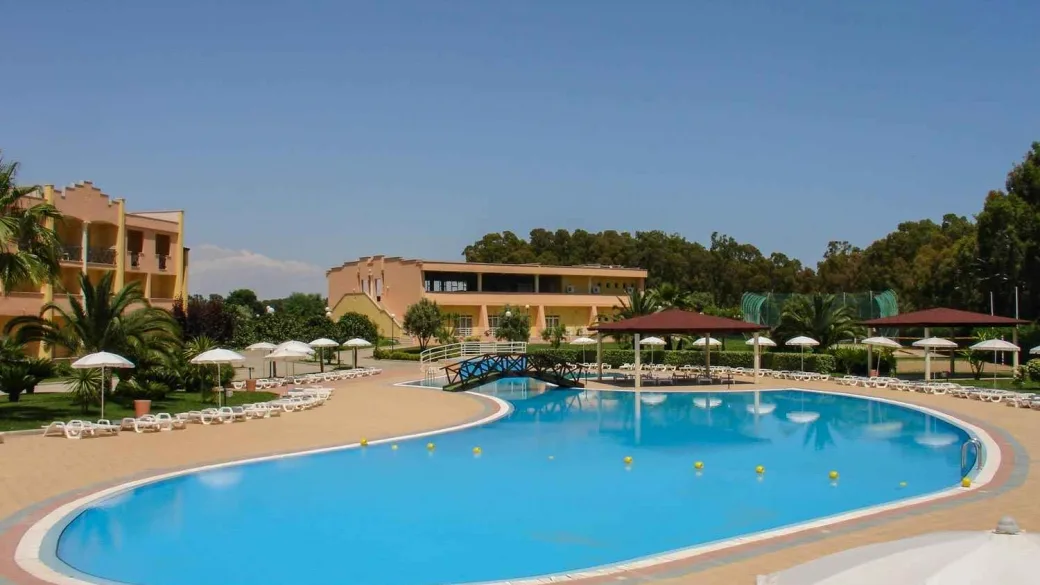 Piscina con ombrelloni bianchi e lettini davanti agli edifici del resort