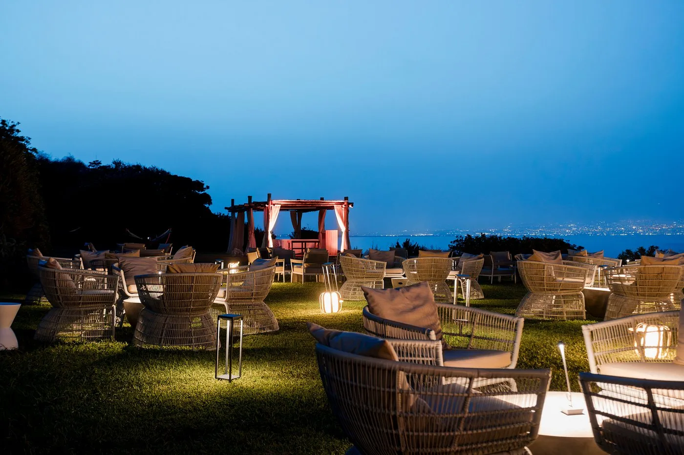Lounge esterna serale con poltrone in rattan e vista sulle luci della costa