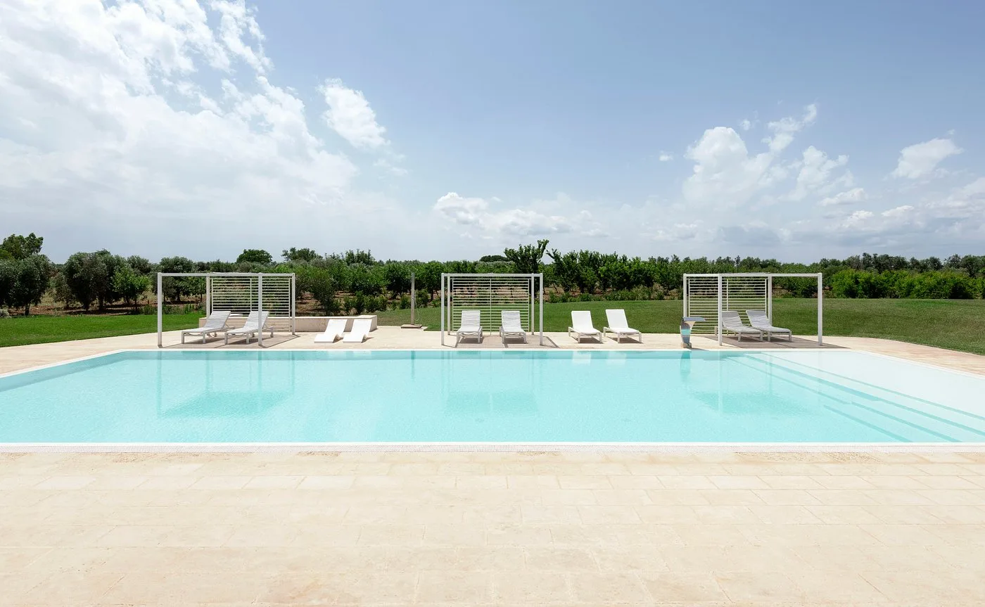 Piscina rettangolare con lettini e gazebo circondata da ulivi e campagna