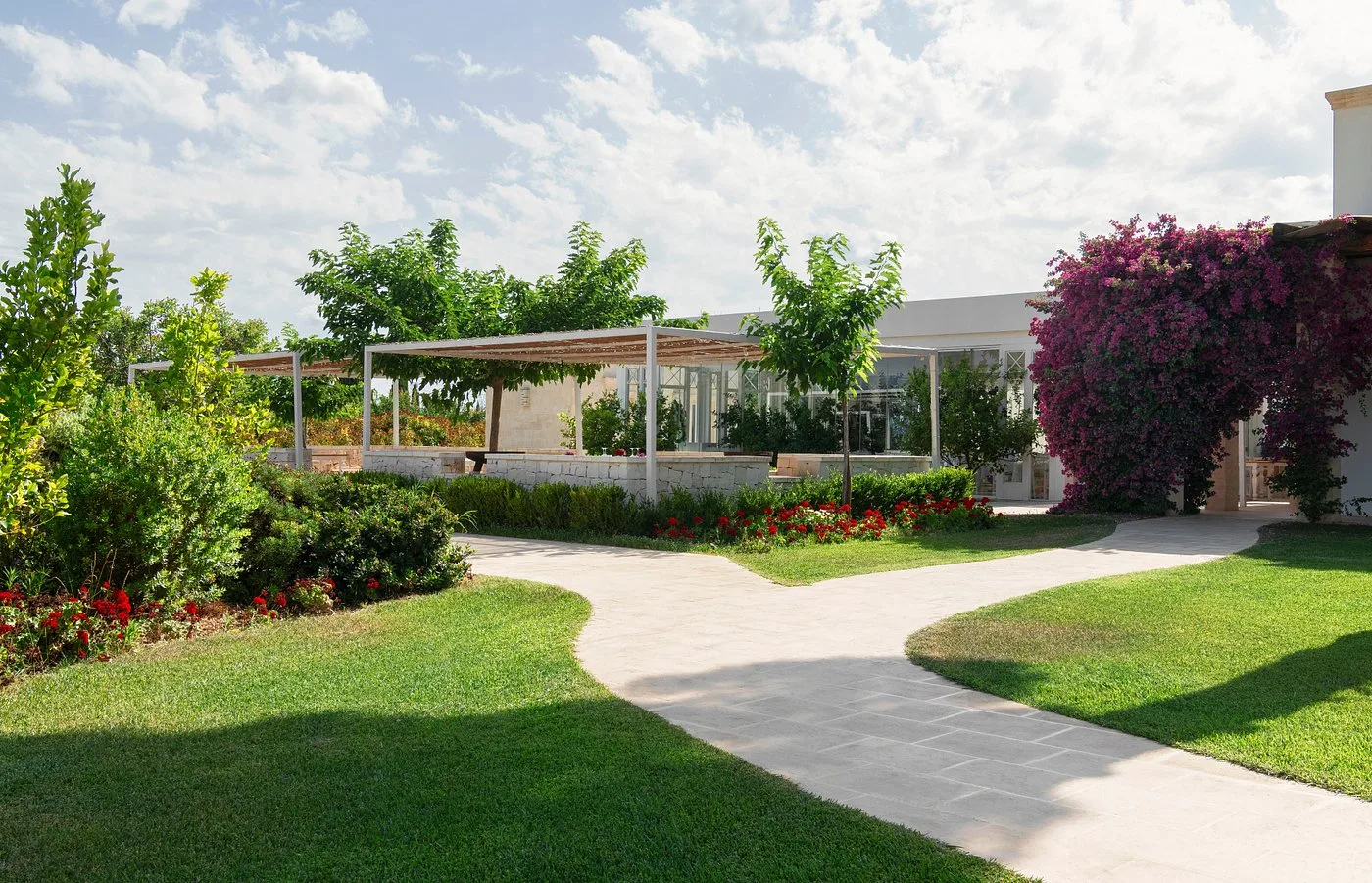 Giardino curato con vialetti, fiori rossi e veranda vetrata della struttura